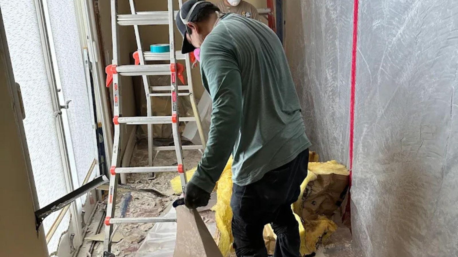 Technician removing wet insulation and drywall during water damage repair