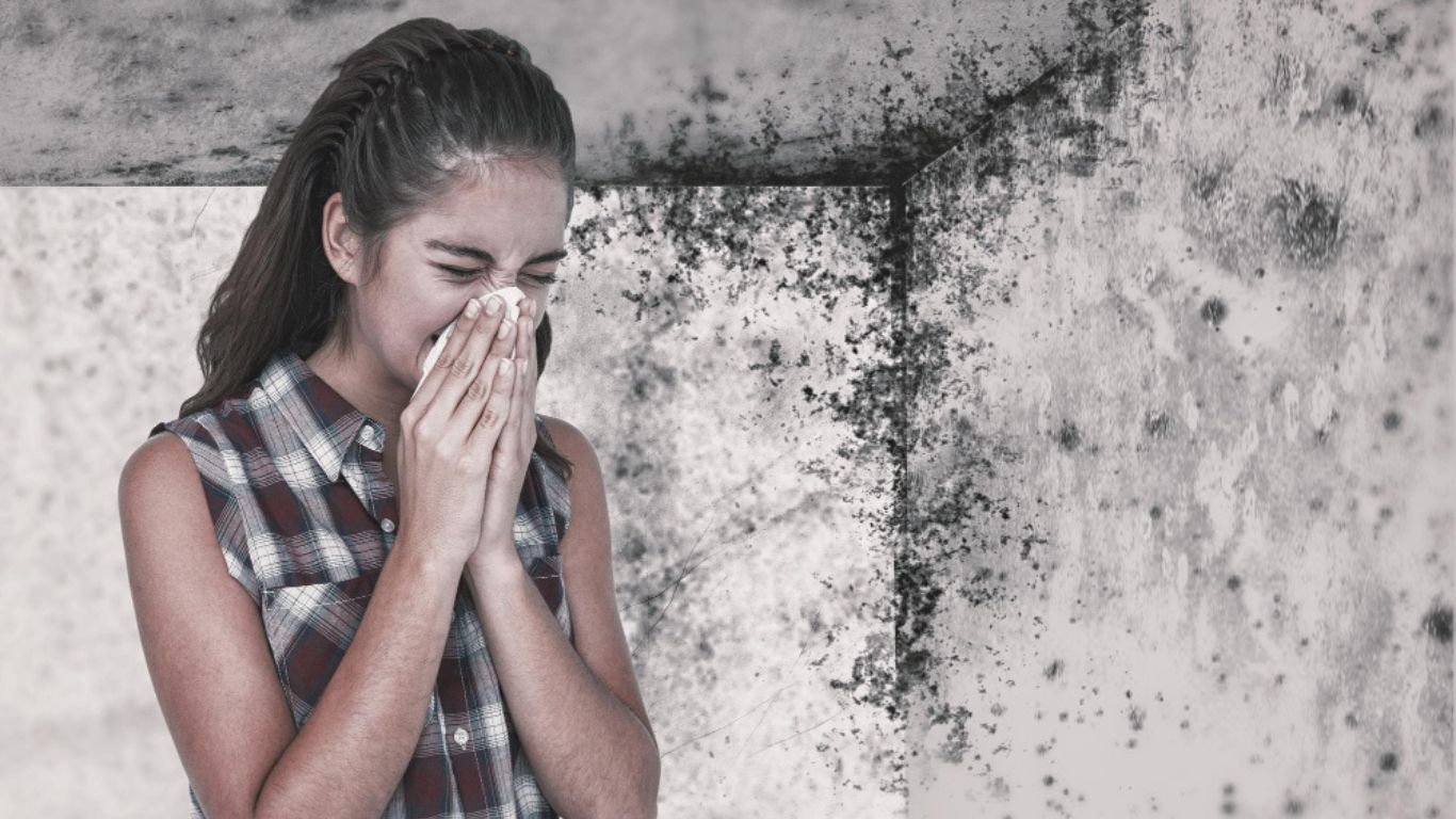 a woman sneezes, experiencing the health risks of mold present in the background